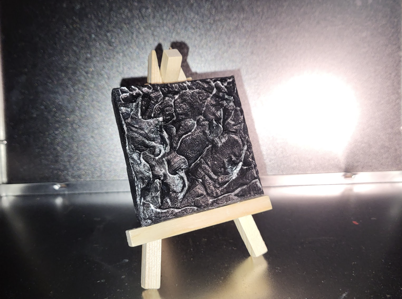 Black textured artwork on a miniature wooden easel